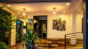 Eine moderne Hotelhalle mit Schachbrettmuster-Boden, Topfpflanzen, Zebra-Kunstwerk und einer Treppe.