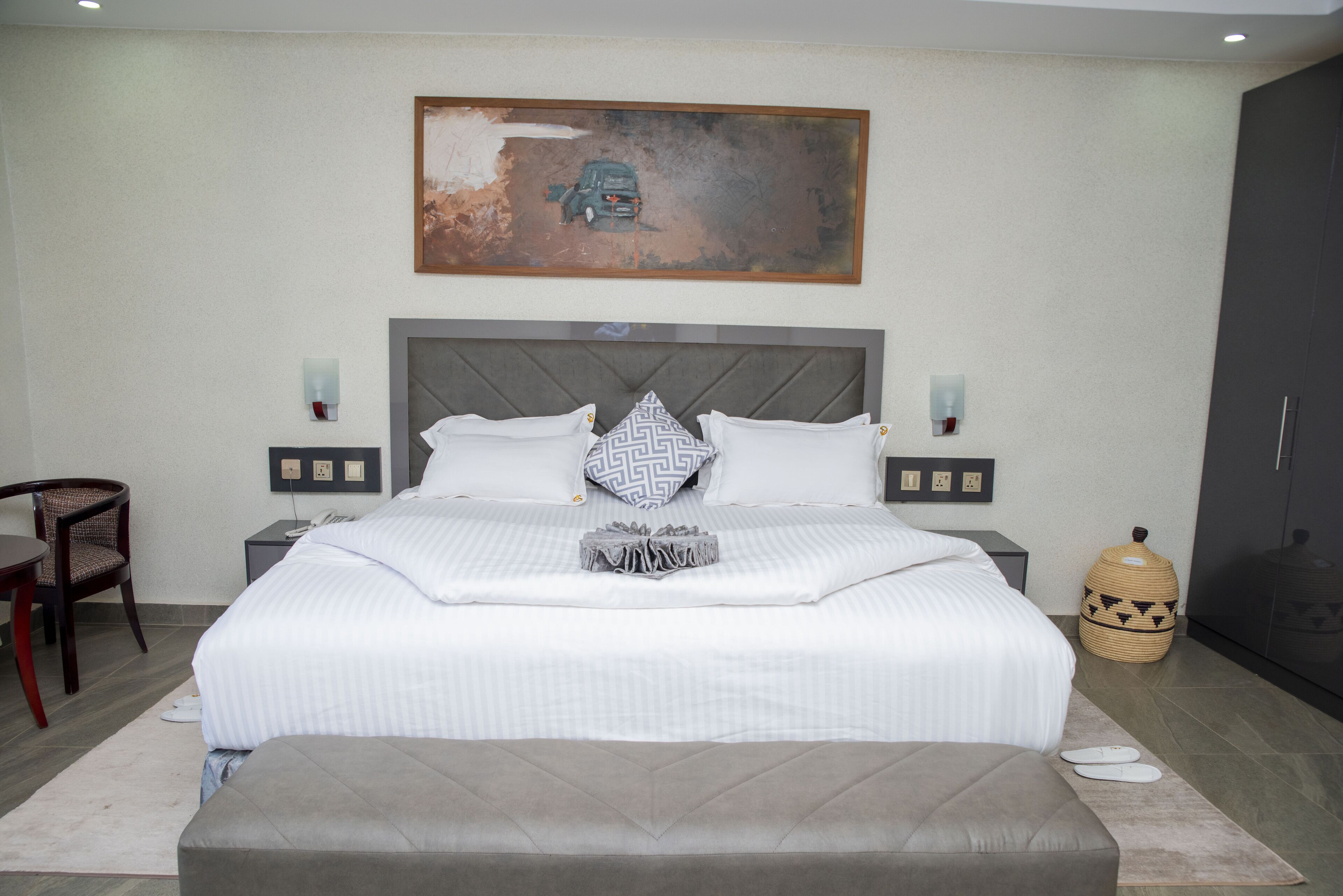 Una camera da letto ordinata con un letto grande, comodini, una sedia, un armadio e un quadro appeso al muro.