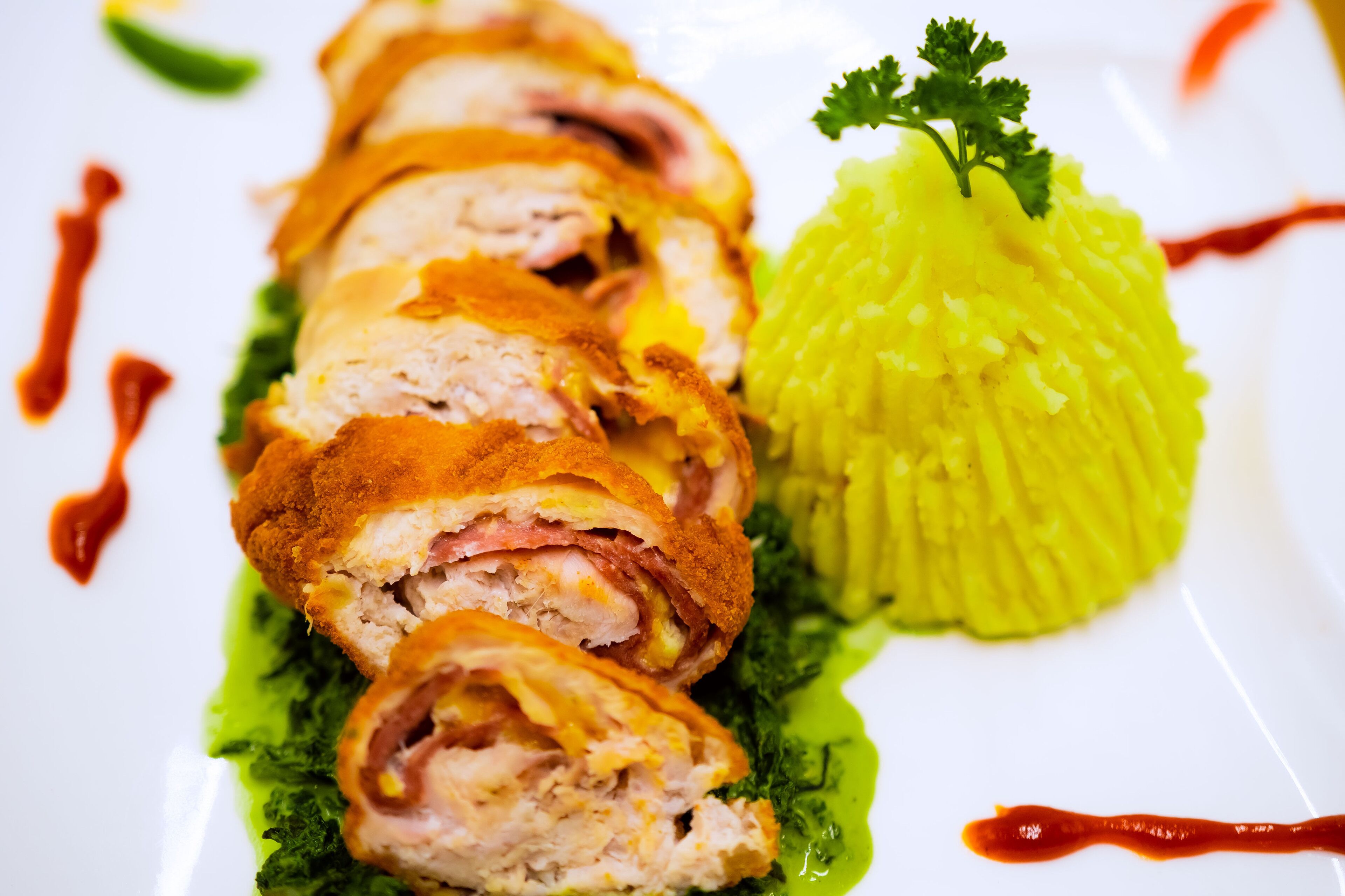 A dish with sliced meat rolls, green sauce, and a garnish on a white plate.