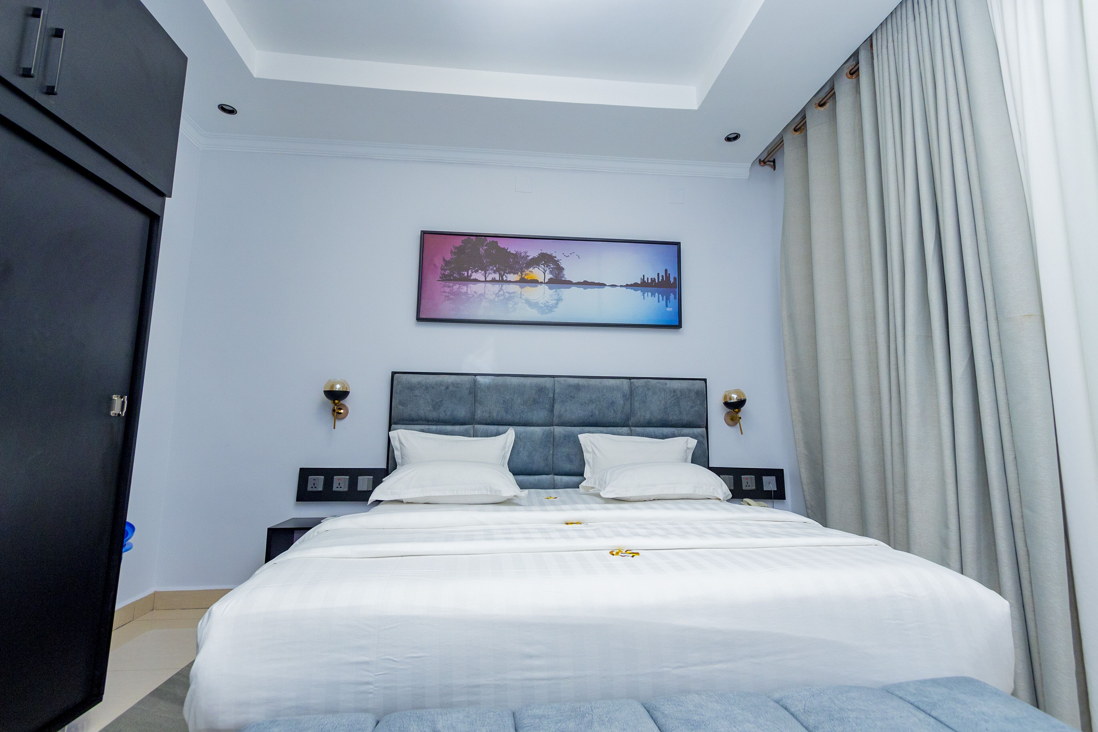 Un dormitorio con una cama grande, un cabecero, un cuadro en la pared y una ventana con cortinas.