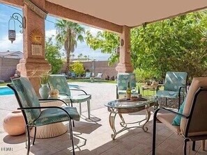 Una terrazza esterna con tavoli e sedie dal piano in vetro, una piscina e vista su palme e case.