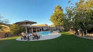 Ein Garten mit Schwimmbad, Kunstgrasanlage und Gartenmöbeln.