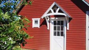 Un bâtiment rouge avec une porte et des fenêtres blanches, entouré de verdure.