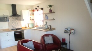 Un espace de vie compact comprenant une cuisine, deux fauteuils en cuir rouge, une petite table en bois et une lampe rouge.