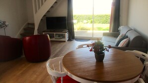 Un salon avec une table à manger en bois, des chaises blanches, un canapé rouge, un canapé gris et un escalier menant à un autre niveau.