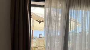 A room with a large window covered by sheer curtains, a wooden floor, and a view of an outdoor patio area with a table and chairs. - Lagom Hotel Seferihisar (Seferihisar)