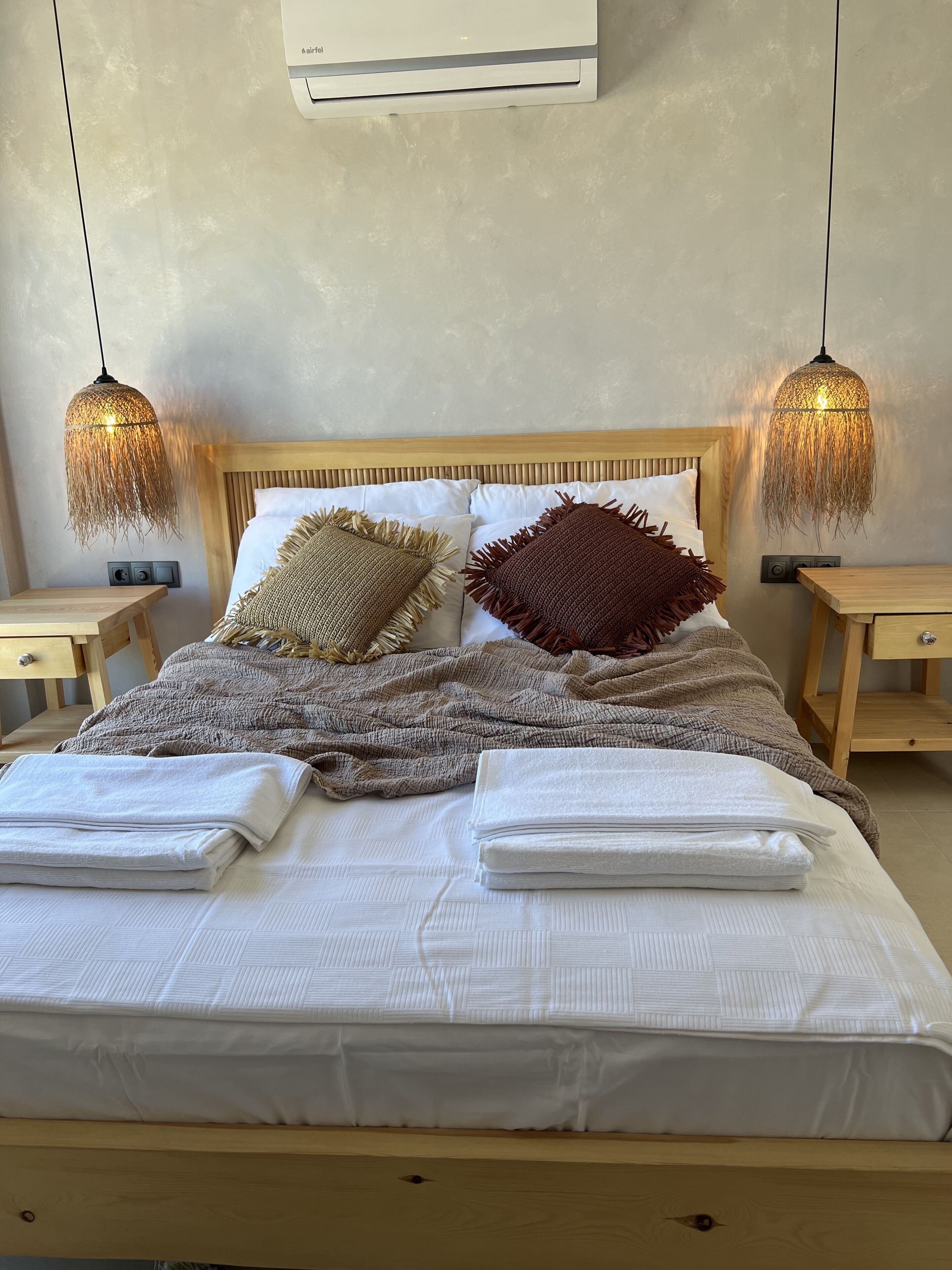 Una cama bien hecha con cabecera de madera, dos mesitas de noche y un aire acondicionado instalado en la pared.