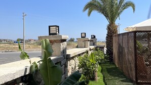 A garden with a palm tree, a stone wall, and a metal fence. - Lagom Hotel Seferihisar (Seferihisar)