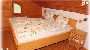 Puinen huone, jossa on sänky, pieni puinen yöpöytä ja ikkuna.