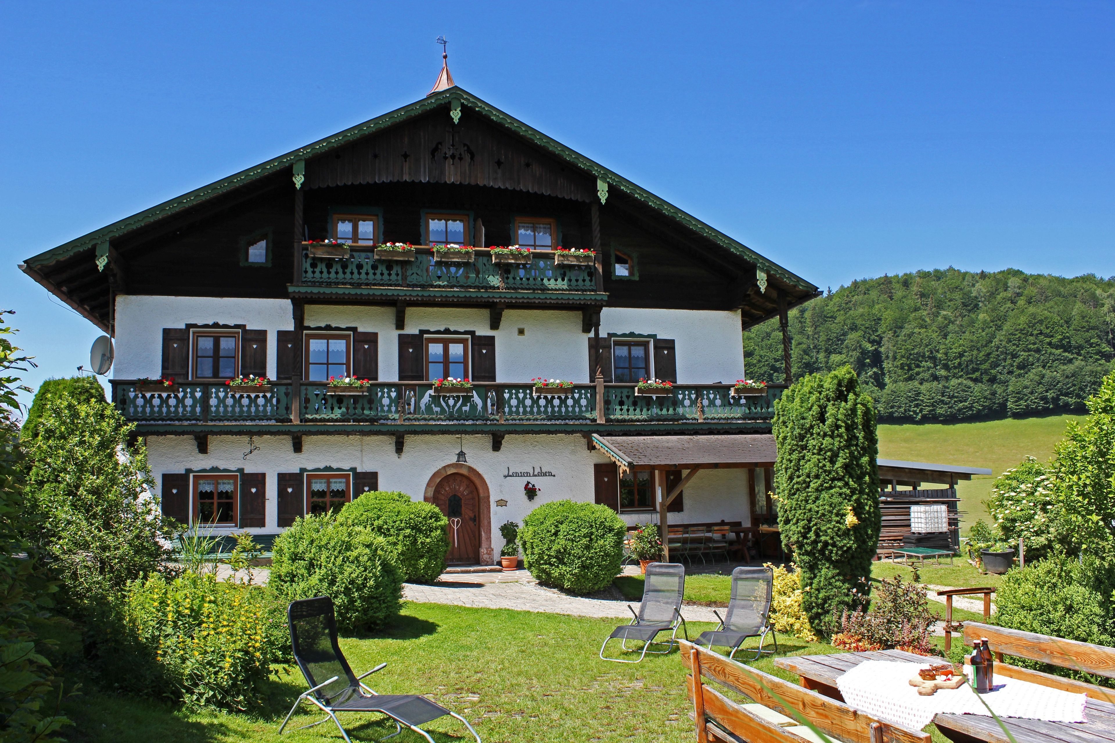 A two-story building with a balcony, a door, and a small garden area with chairs and tables.
