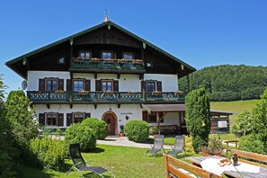 A two-story building with a balcony, a door, and a small garden area with chairs and tables. - Ferienwohnung Watzmann (Marktschellenberg)