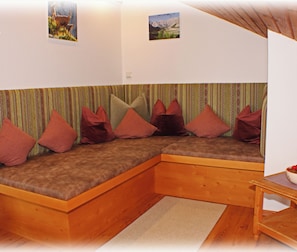 A cozy room with a wooden bench seating area, a small table with a bowl of fruit, and two framed pictures on the wall.