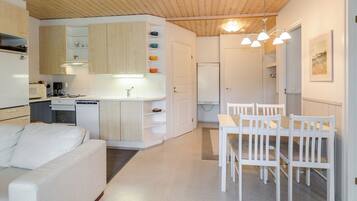 A modern kitchen with white cabinets, a dining table with chairs, and a white sofa in a bright room with wooden ceiling beams.