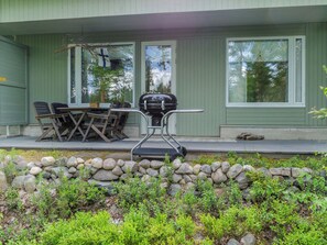 A covered outdoor seating area with a grill, a stone wall, and a view of the surrounding greenery.