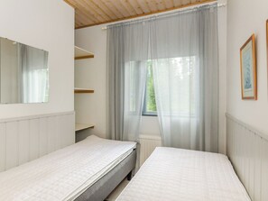 Une chambre avec deux lits, une fenêtre avec des rideaux légers, un radiateur et un miroir au mur.