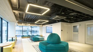 A modern office space with a teal sofa, wooden tables, and a striped rug. - Prince Smart Inn Hakata (Fukuoka)