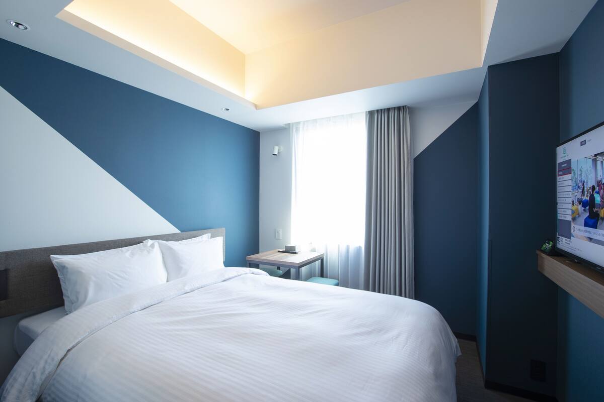 A modern hotel room with a neatly made bed, a small table, and a TV on a stand.