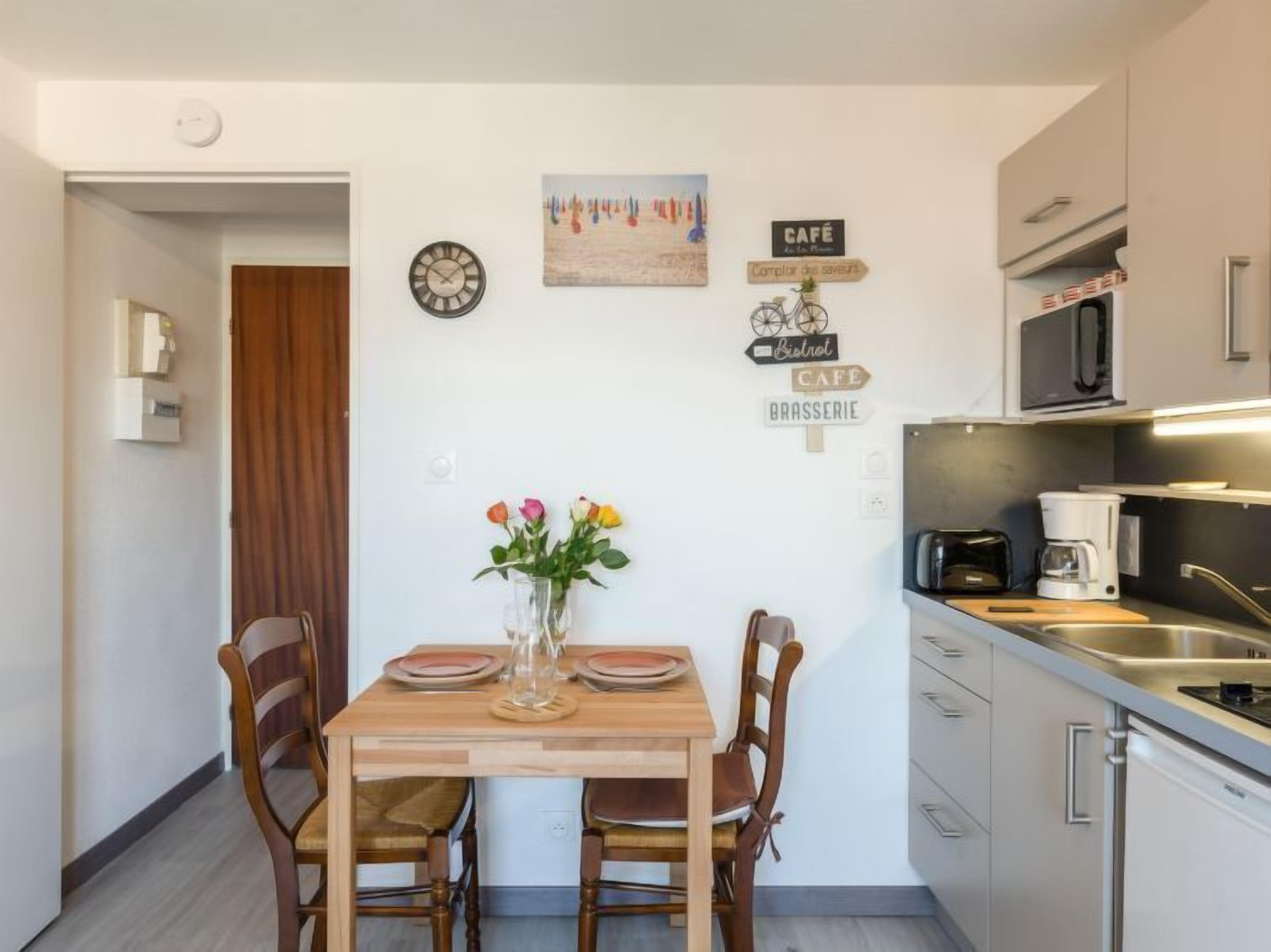 Une cuisine compacte avec un coin repas, une horloge et des éléments de décoration murale, notamment des panneaux indiquant « CAFÉ » et « BRASSERIE ».