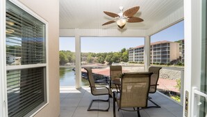 A balcony with a table and chairs, a ceiling fan, and a view of a body of water and buildings.