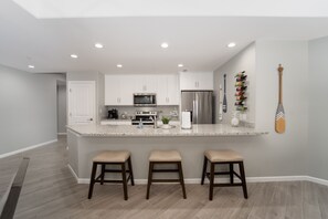 Une cuisine moderne avec des meubles blancs, un îlot central doté de tabourets, un four à micro-ondes, un réfrigérateur et un décor mural en bois en forme de pagaie.
