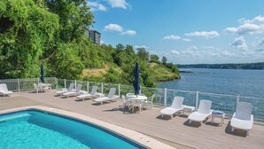 A poolside area with lounge chairs and a table, overlooking a body of water.