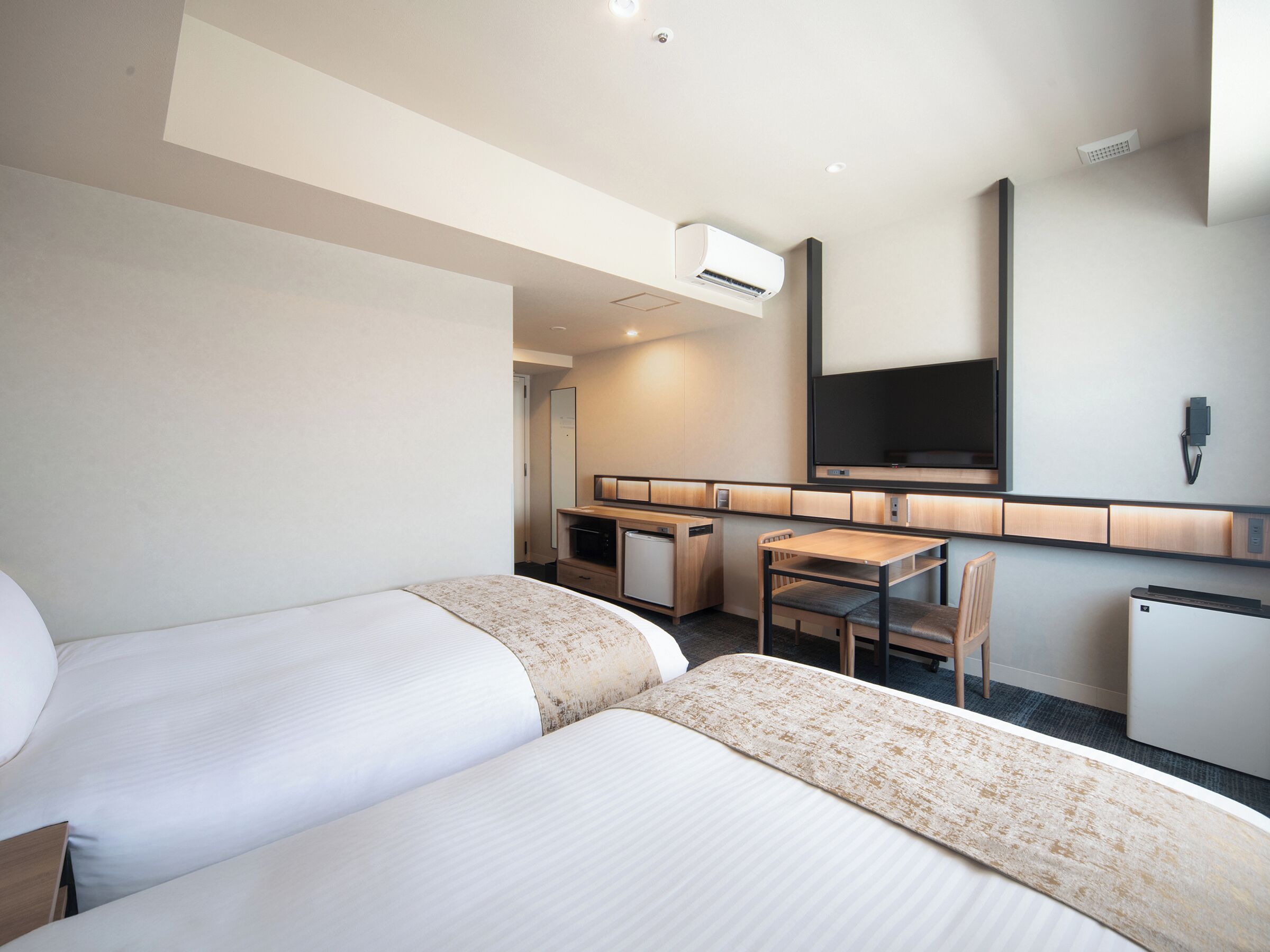 A hotel room with two beds, a desk, a chair, a television, and a small refrigerator.