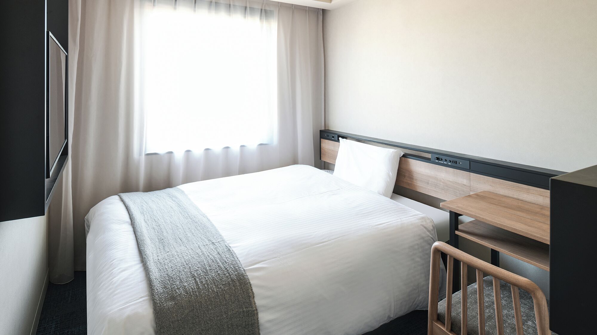 A hotel room with a bed, bedside table, and a window with curtains.