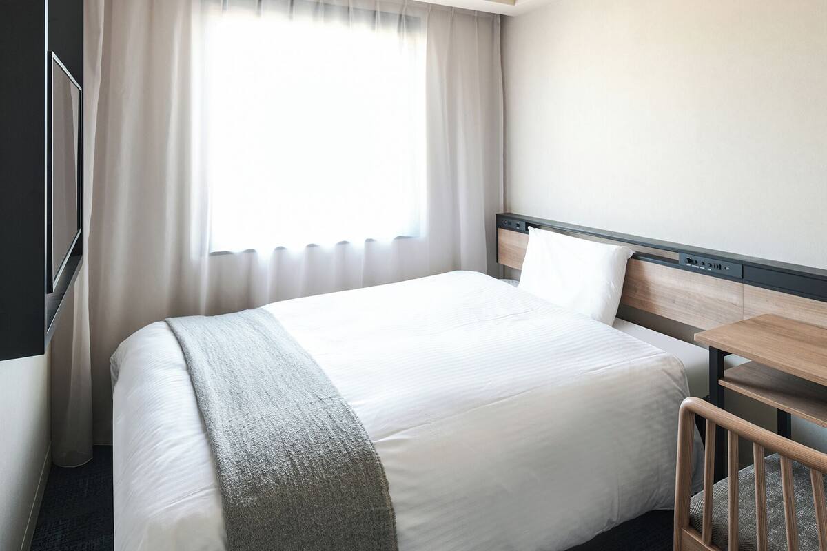 A hotel room with a bed, bedside table, and a window with curtains.