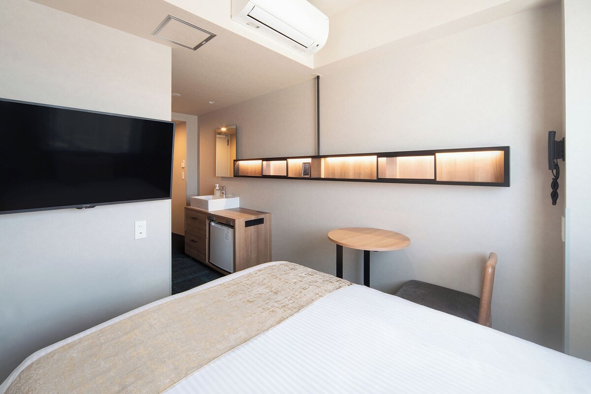 Una habitación de hotel con una cama, televisión, una mesita, escritorio y espejo.