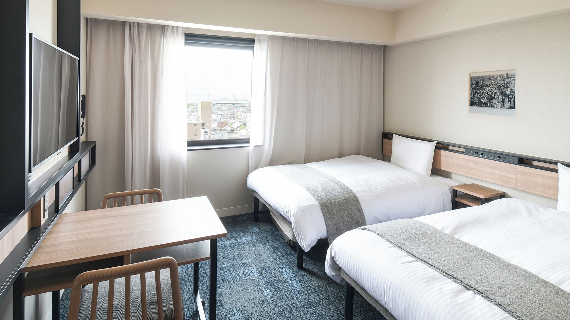 A hotel room with two beds, a desk, a chair, a TV, and a window with curtains.