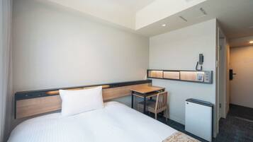 A hotel room with a bed, a desk, a chair, a small table, and a wall-mounted phone.