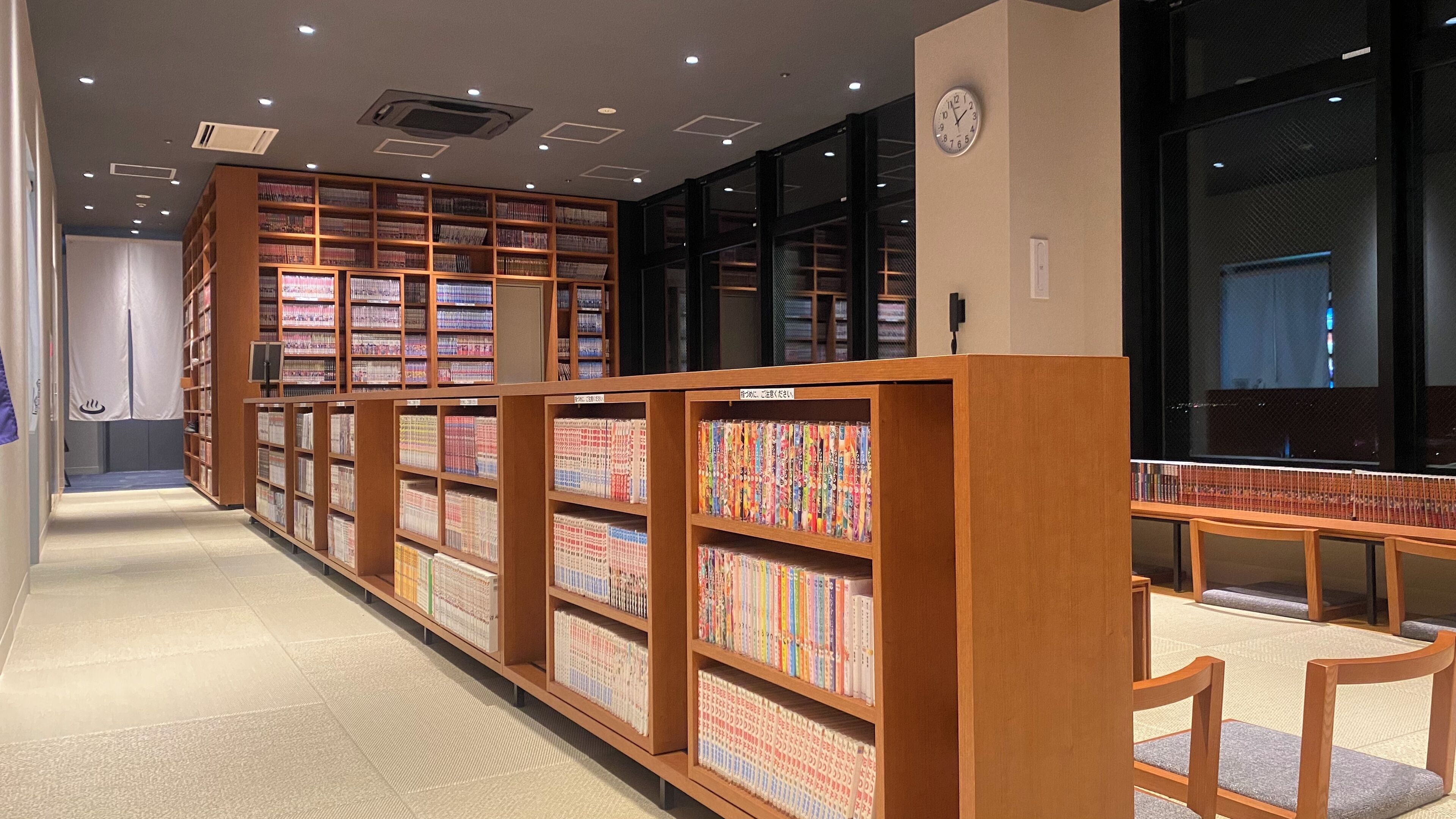 A library with wooden bookshelves and a clock on the wall.
