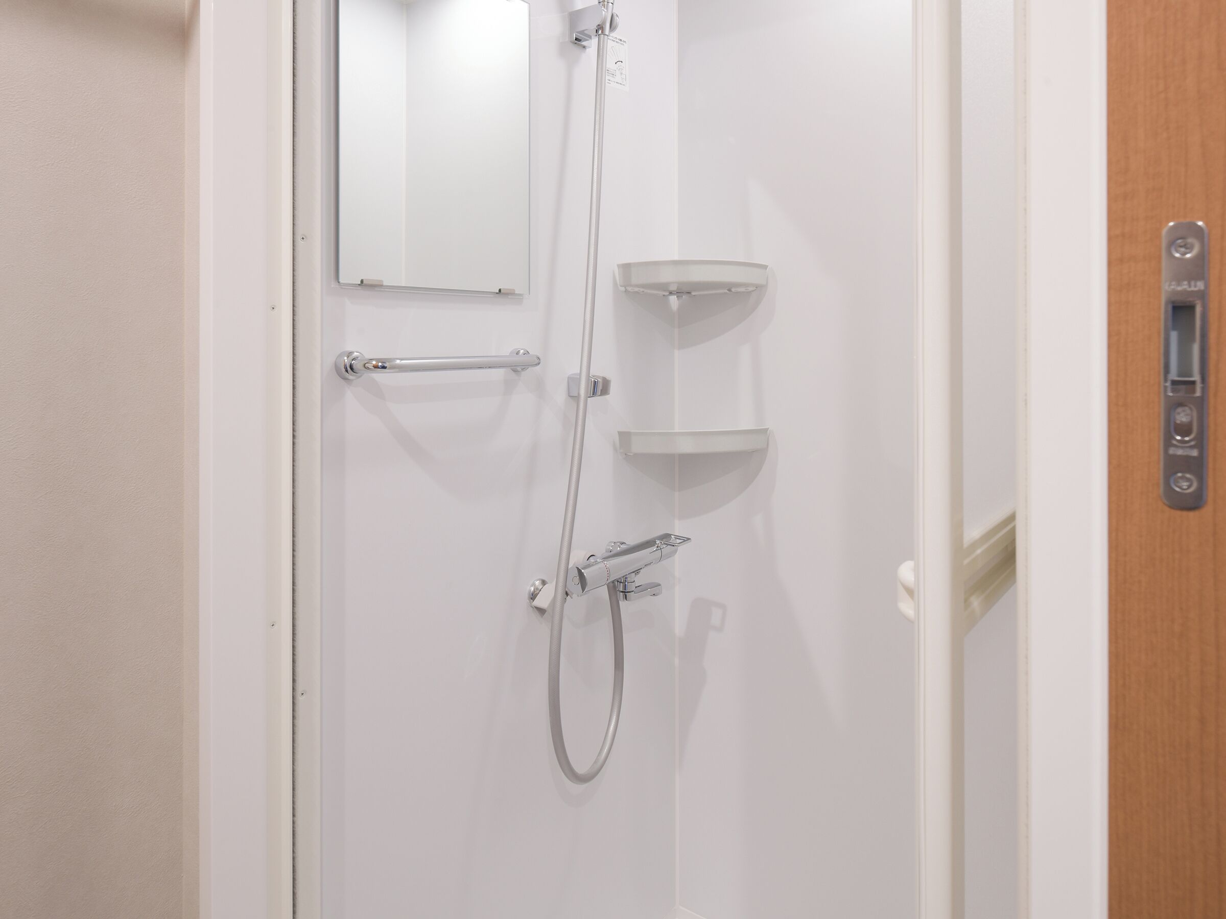 Una porta blanca amb dutxa, penjador de tovalloles i una petita prestatgeria.