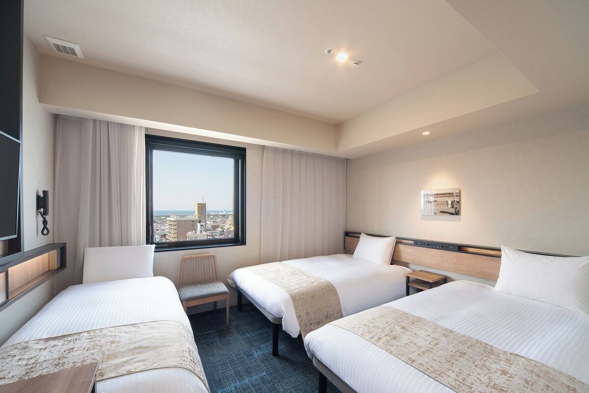 A hotel room with two beds, a desk, a chair, a window with a city view, and a mounted phone.