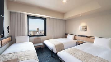 A hotel room with two beds, a desk, a chair, a window with a city view, and a mounted phone.