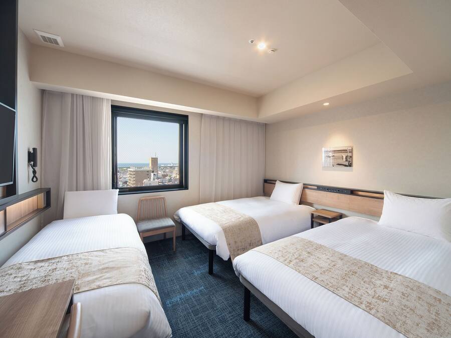 A hotel room with two beds, a desk, a chair, a window with a city view, and a mounted phone.