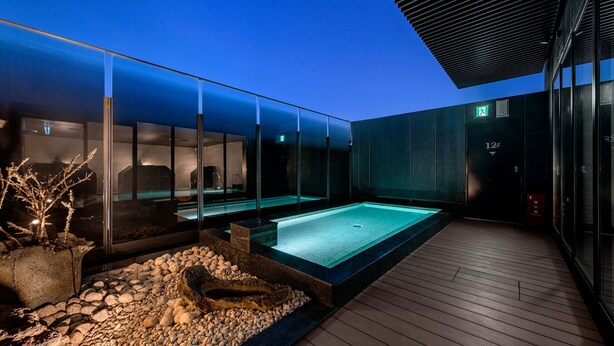 Un espace piscine extérieur moderne, doté de parois en verre, d’une terrasse en bois et d’un élément décoratif en pierre.