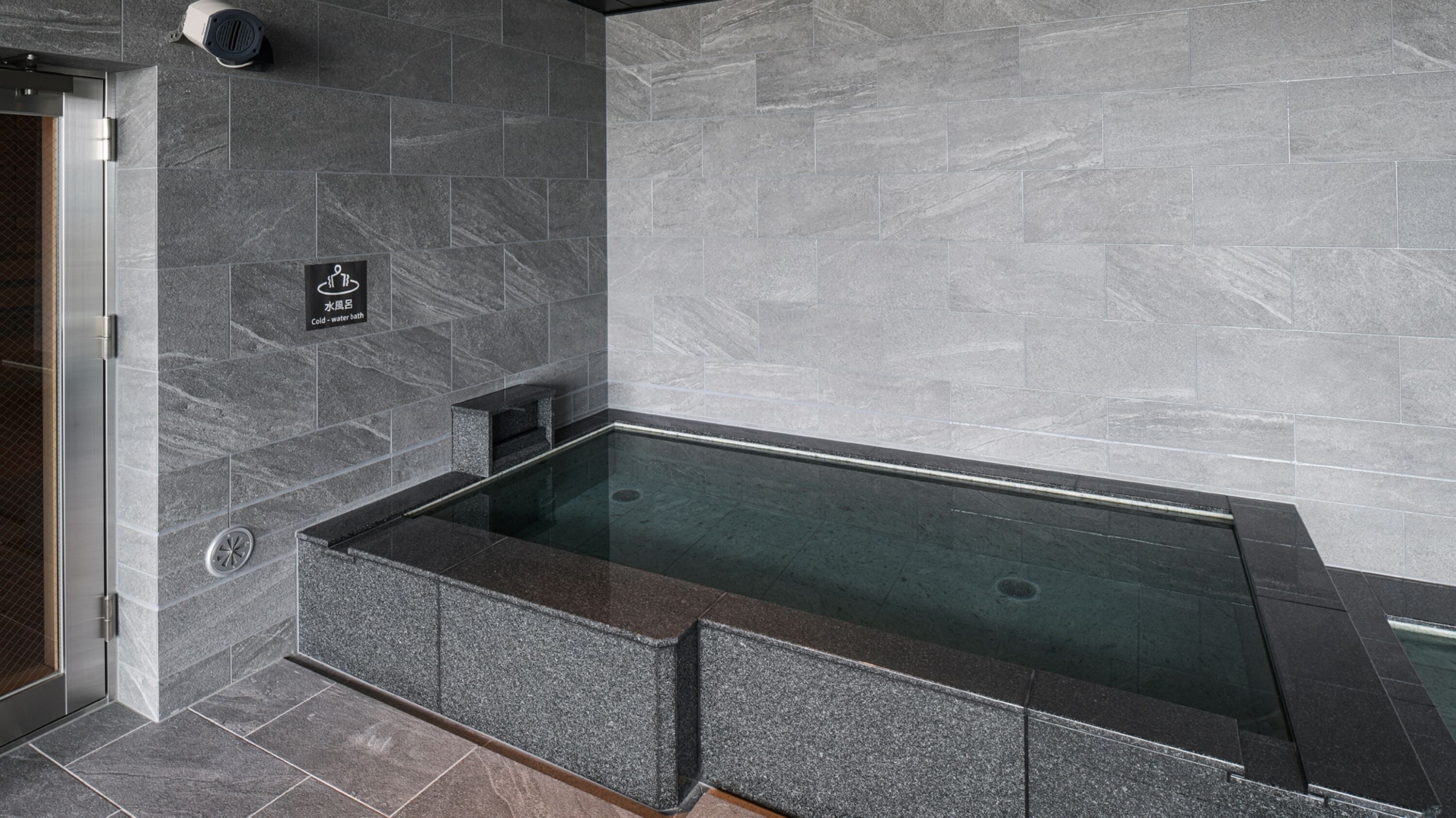 A modern bathroom with a glass-enclosed hot tub, grey marble tiles, and a cold-water bath sign.