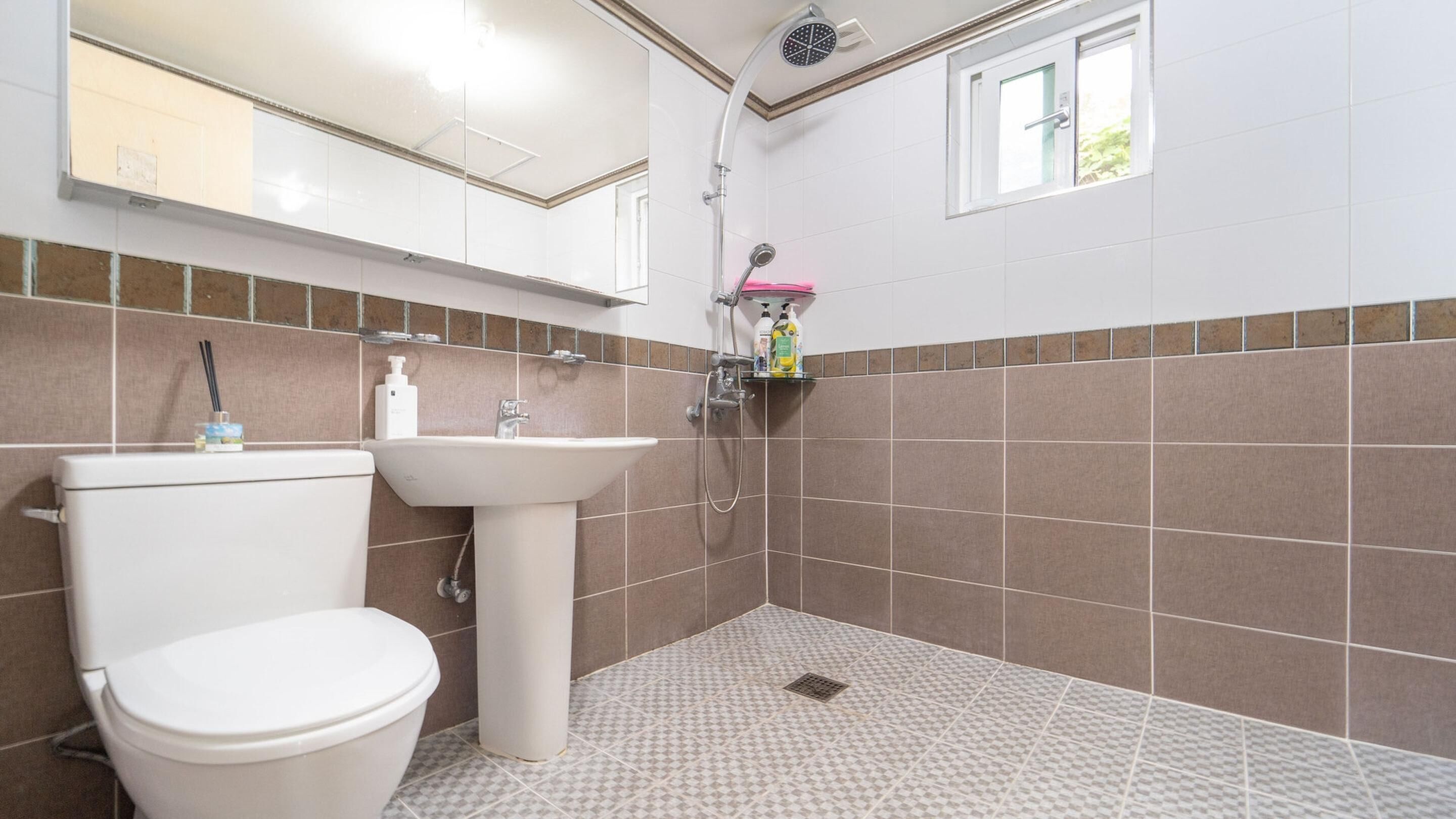 A bathroom with a toilet, sink, shower, and tiled walls.