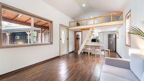Amplia sala de estar con piso de madera, una escalera que conduce a un altillo y una cocina con refrigerador.