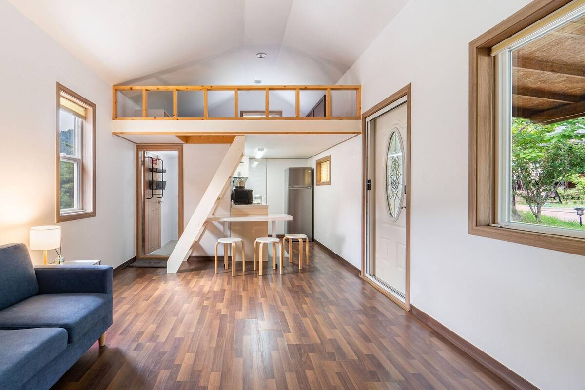 Un interior moderno con un dormitorio entrepiso, una zona de comedor y una sala de estar con sofá y lámpara.