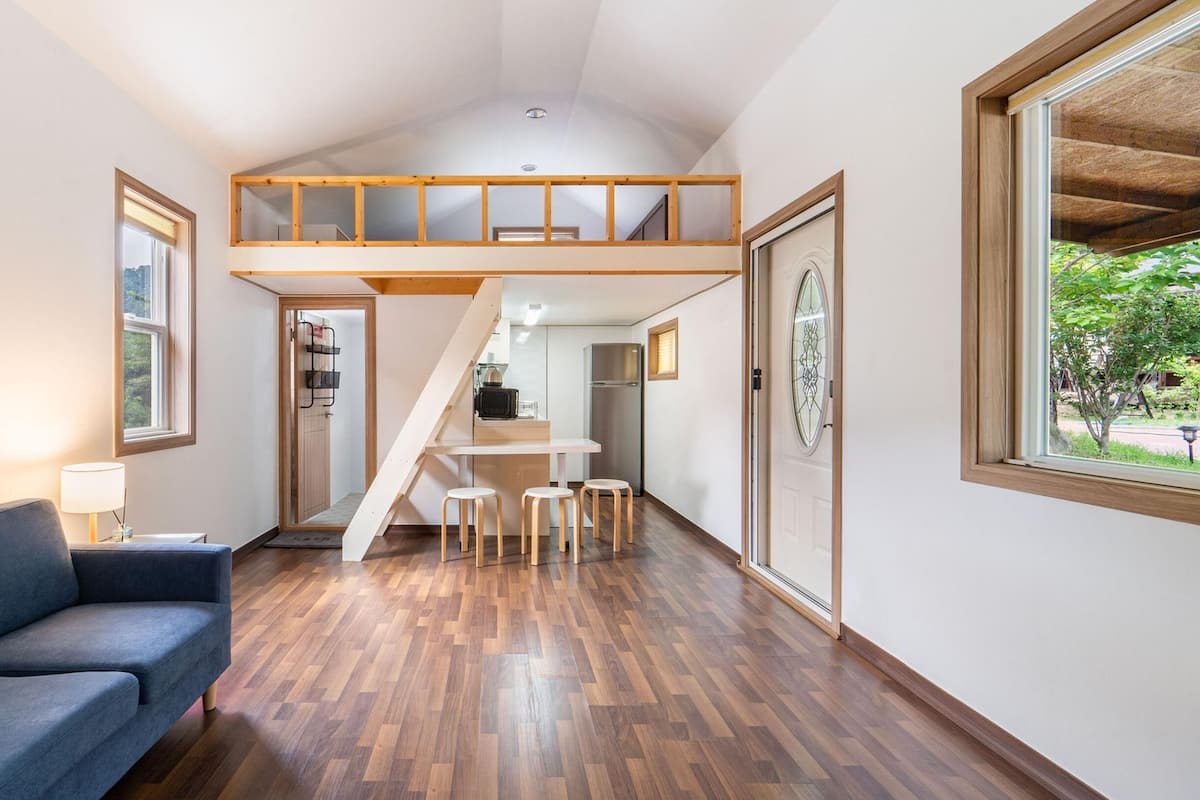 A modern interior with a loft bedroom, a dining area, and a living room with a sofa and a lamp.