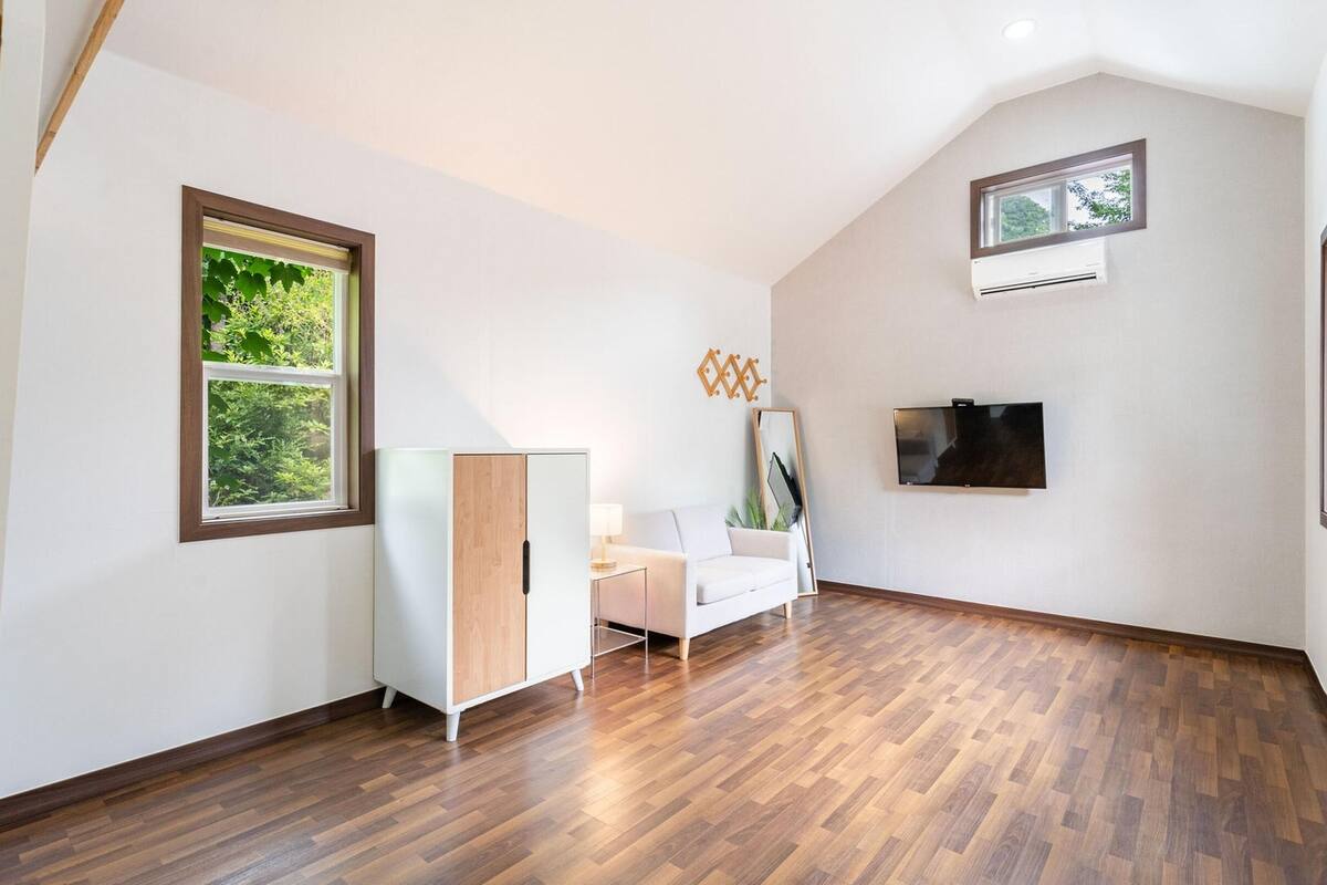 Una habitación moderna y luminosa con suelo de madera, un sofá blanco, una mesita y un televisor montado en la pared.