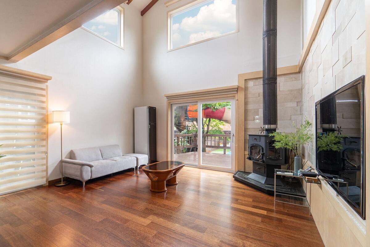 Un amplio salón con piso de madera, un sofá, una mesa de centro, una chimenea y un ventanal corredizo que da a una terraza exterior.