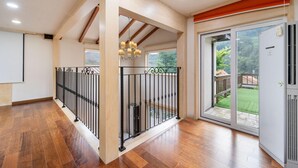 Un pasillo espacioso con piso de madera, baranda de metal negro y puerta corredera de vidrio que da a un jardín.