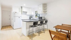 Une cuisine moderne avec des meubles blancs, un plan de travail noir et une table à manger en bois, accompagnée de chaises.