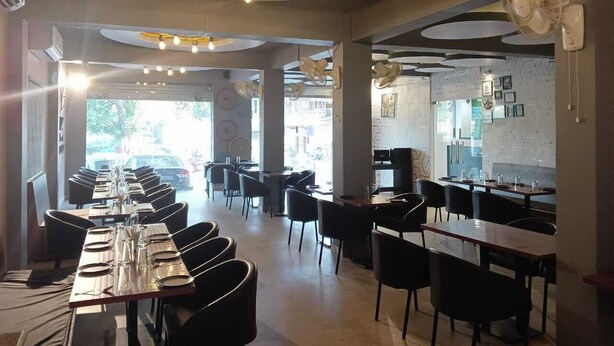 Un intérieur de restaurant moderne, doté de nombreuses tables et chaises, de luminaires originaux au plafond et de grandes fenêtres laissant entrer la lumière naturelle.