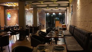 Un restaurant avec un long comptoir, des chaises noires et un panneau lumineux au néon sur le mur.