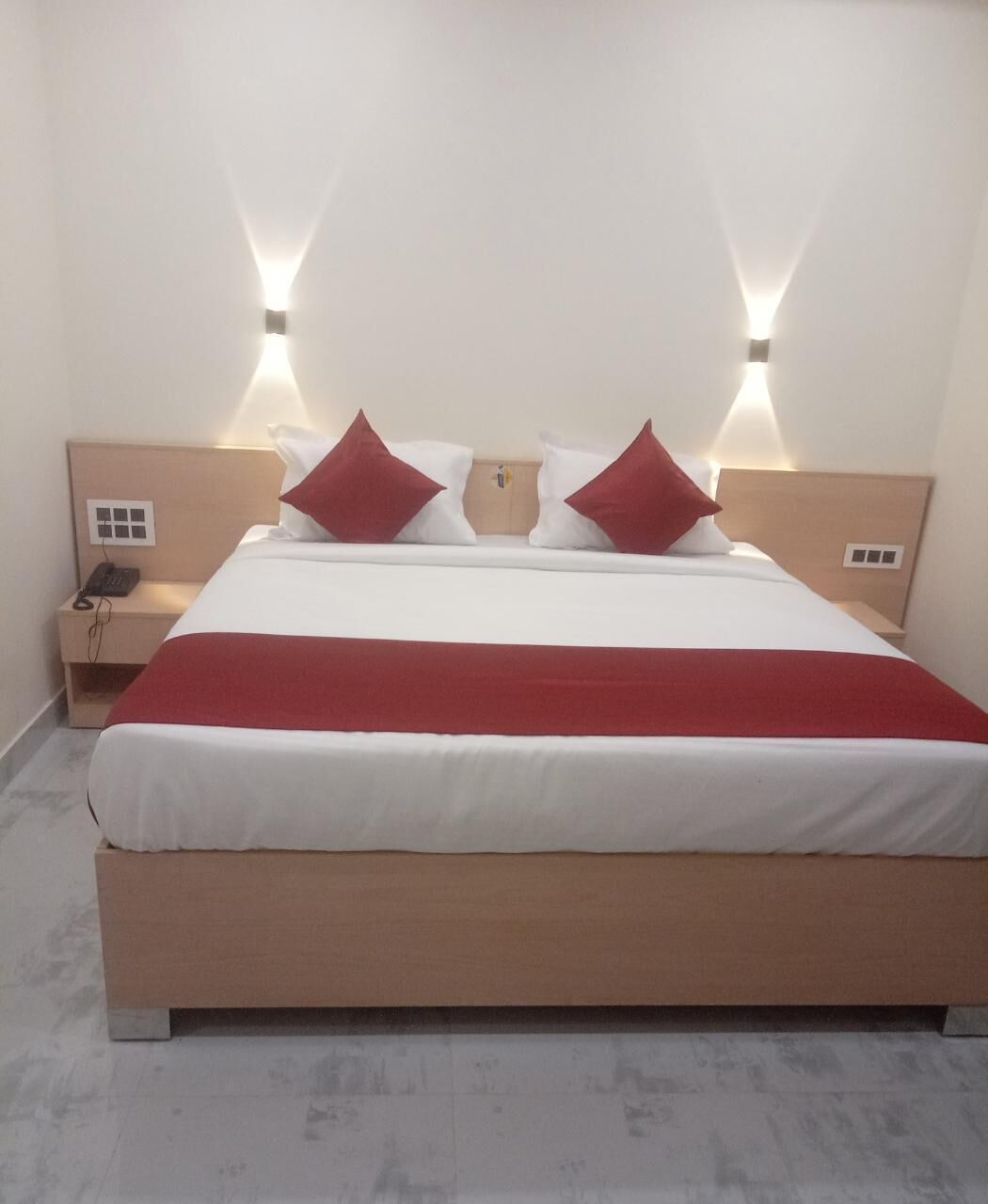 Un letto rifatto con copriletto rosso e bianco, due cuscini rossi e due abat-jour su comodini in legno.