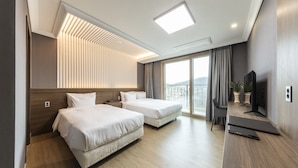 Habitación de hotel con dos camas, un escritorio con televisor, una silla y un balcón con vistas.
